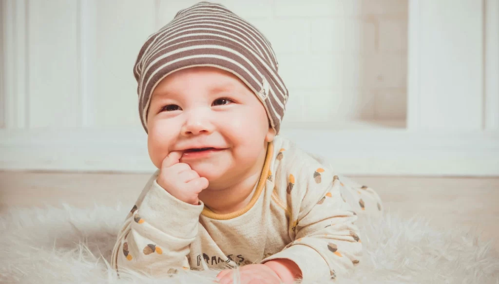 infant with finger in mouth smiling 